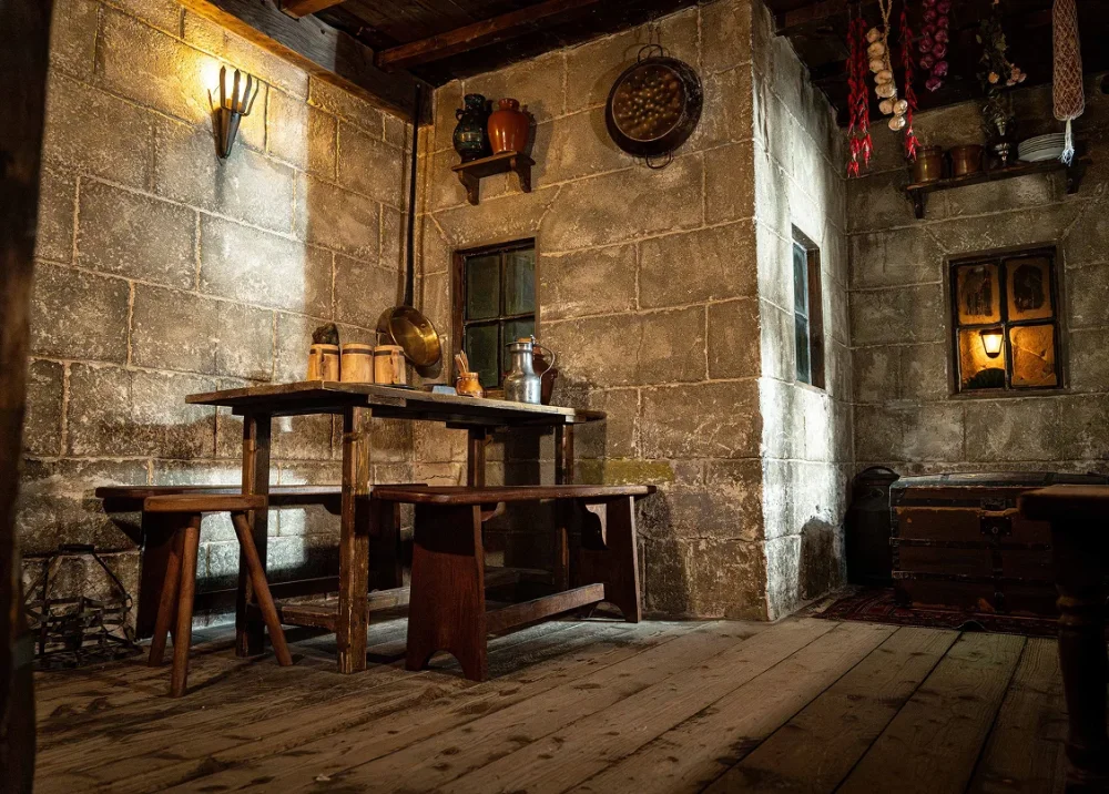 Inside a medieval inn with stone walls, a long wooden table and a lit window
