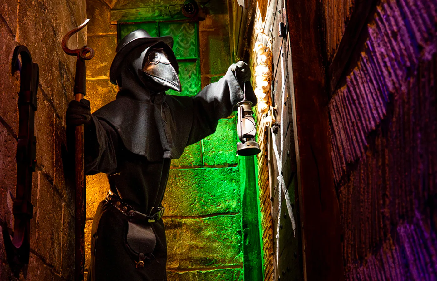 Medieval alley lit in green and purple, where a masked plague doctor holds a lantern